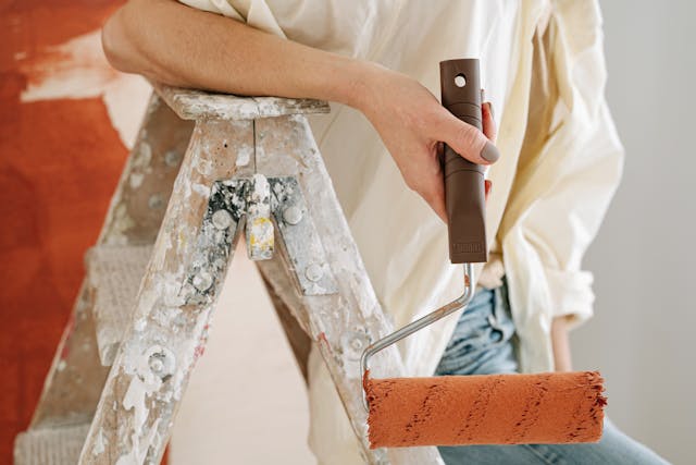 Person leaning on a ladder holding a paint roller